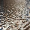 Zbliżenie na połyskujący panel WPC o srebrnej strukturze, który odbija niebieskie i miedziane refleksy światła