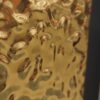 Bliskie ujęcie złotej, metalicznej faktury o nieregularnych zagłębieniach i odbiciach, charakterystycznej dla płyty węglowej matowej w wariancie metalicznym.